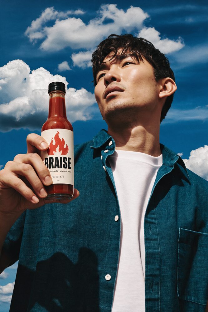 Affiche BRAISE : un homme tient la bouteille de sauce piquante sous un ciel bleu